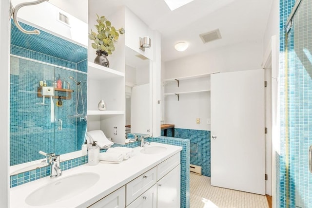 bathroom with tile walls, tile patterned floors, a shower stall, double vanity, and a wainscoted wall
