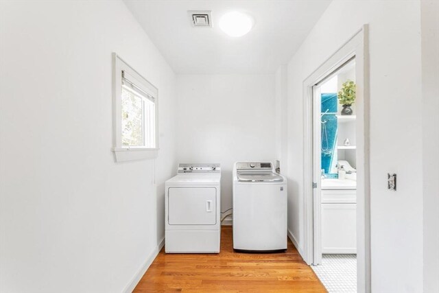 clothes washing area with independent washer and dryer, light wood-style floors, and baseboards