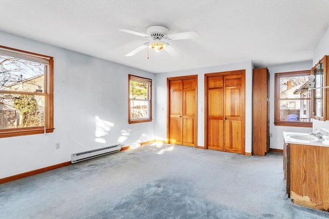 unfurnished bedroom featuring ceiling fan, sink, baseboard heating, light carpet, and two closets