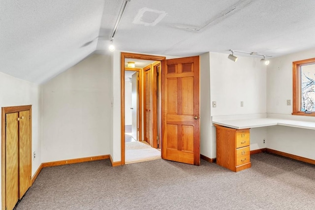 additional living space featuring light colored carpet, lofted ceiling, a textured ceiling, and built in desk