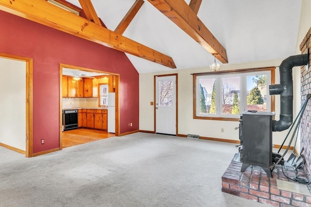 carpeted living room featuring a wood stove, ceiling fan, and lofted ceiling with beams