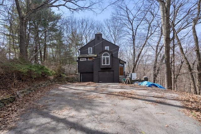 view of side of home with an attached garage, a chimney, and aphalt driveway