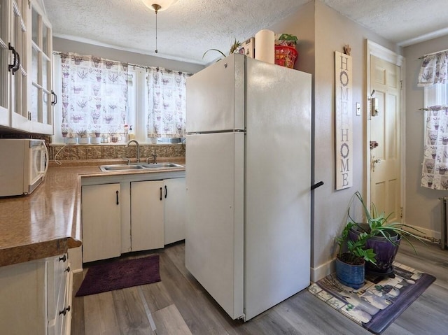 kitchen with white cabinetry, sink, white appliances, and light hardwood / wood-style flooring