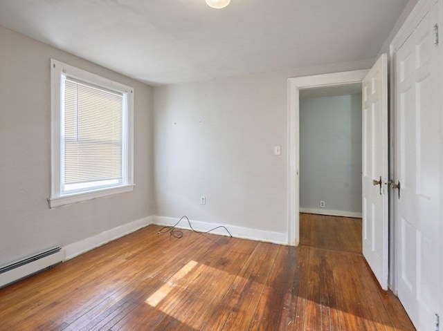 unfurnished room featuring wood-type flooring and a baseboard heating unit