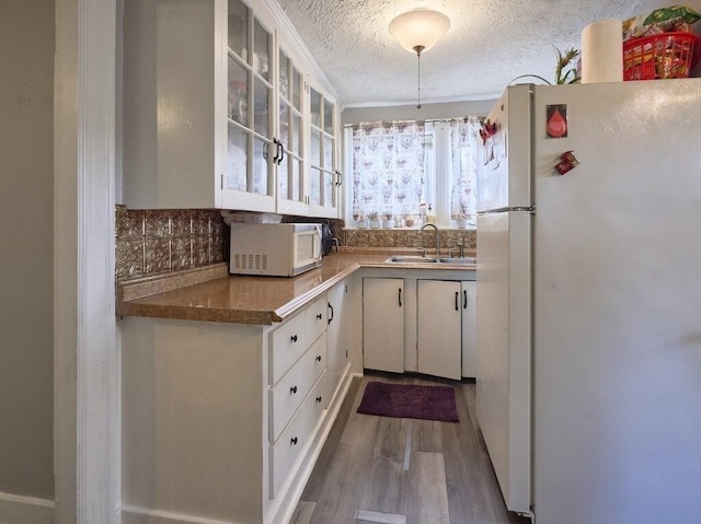 kitchen featuring sink, white cabinetry, wood-type flooring, a textured ceiling, and white appliances