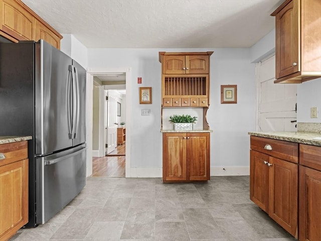 kitchen with freestanding refrigerator, brown cabinets, and light stone countertops