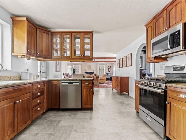 kitchen with a peninsula, open floor plan, arched walkways, a sink, and appliances with stainless steel finishes