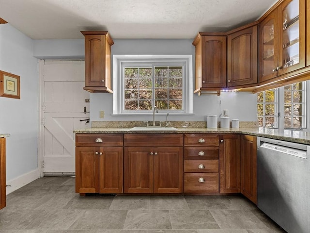 kitchen featuring stainless steel dishwasher, brown cabinetry, glass insert cabinets, light stone counters, and a sink
