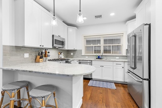 kitchen with pendant lighting, dark hardwood / wood-style flooring, light stone counters, white cabinetry, and stainless steel appliances