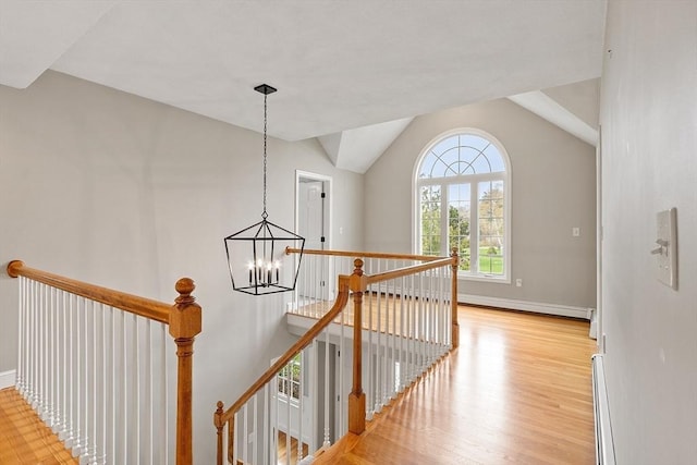 hall with a notable chandelier, an upstairs landing, baseboard heating, and light wood-style flooring