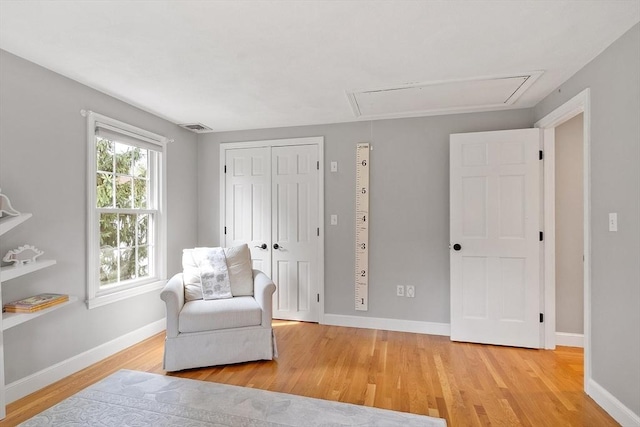 sitting room with baseboards, attic access, light wood-type flooring, and visible vents