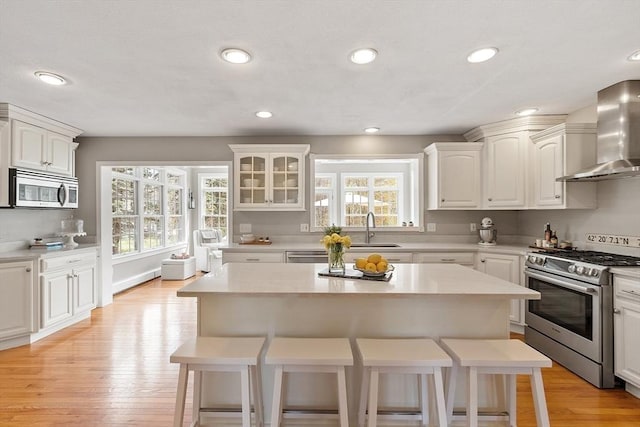 kitchen featuring wall chimney range hood, a breakfast bar area, appliances with stainless steel finishes, a sink, and light countertops