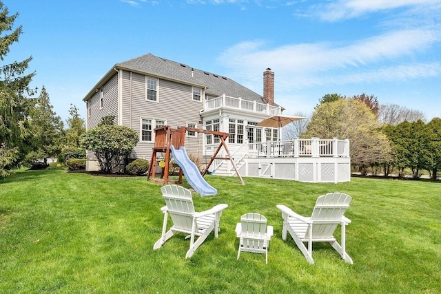 back of house with a playground, a wooden deck, a chimney, a balcony, and a lawn