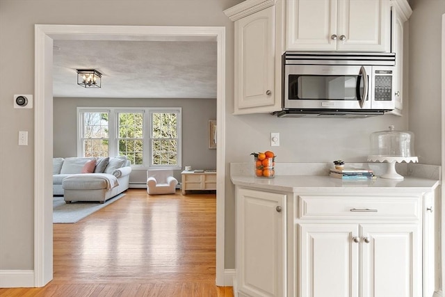 kitchen featuring light countertops, stainless steel microwave, a baseboard radiator, and light wood-style floors