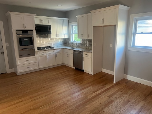 kitchen with backsplash, white cabinets, sink, light hardwood / wood-style flooring, and stainless steel appliances