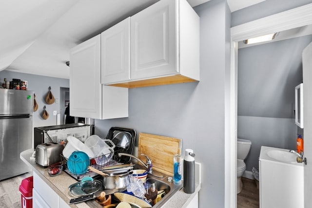 kitchen featuring wood-type flooring, stainless steel fridge, and white cabinetry