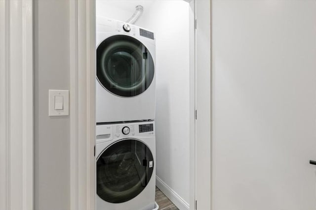 laundry area featuring estacked washer and dryer, wood finished floors, and baseboards