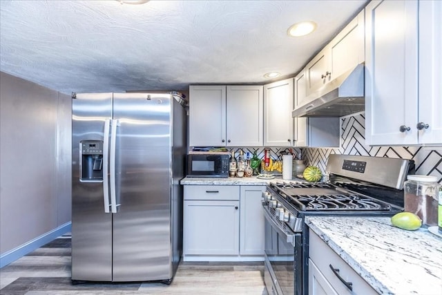 kitchen featuring light stone counters, backsplash, light hardwood / wood-style flooring, and appliances with stainless steel finishes