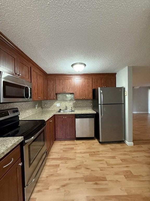 30 Revere Beach Pkwy Unit 116, Medford, MA 02155 - kitchen featuring appliances with stainless steel finishes, a sink, light wood-type flooring, tasteful backsplash, and a textured ceiling