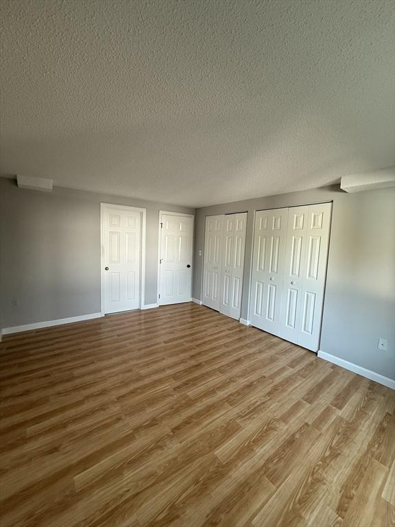 30 Revere Beach Pkwy Unit 116, Medford, MA 02155 - unfurnished bedroom with two closets, wood finished floors, a textured ceiling, and baseboards