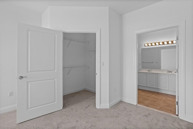 unfurnished bedroom featuring sink, ensuite bath, a spacious closet, light colored carpet, and a closet