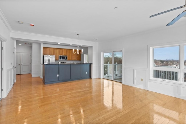 unfurnished living room featuring crown molding, a healthy amount of sunlight, ceiling fan with notable chandelier, and light hardwood / wood-style floors