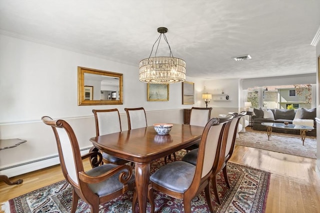 dining room featuring a baseboard heating unit, visible vents, a chandelier, crown molding, and wood finished floors