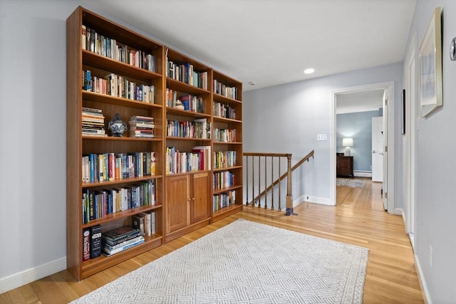 living area with a baseboard heating unit, an upstairs landing, recessed lighting, light wood finished floors, and baseboards