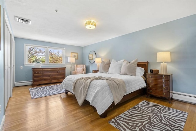 bedroom with baseboards, baseboard heating, visible vents, and wood finished floors