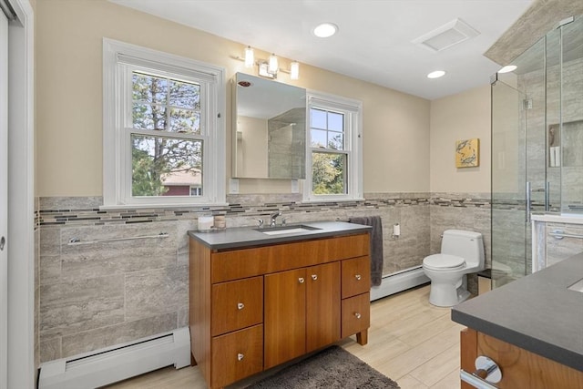 bathroom with tile walls, vanity, toilet, and baseboard heating