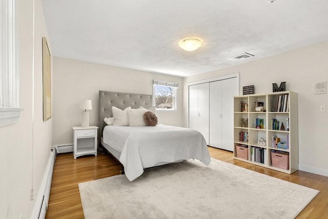 bedroom featuring a closet, baseboards, a baseboard heating unit, visible vents, and wood finished floors