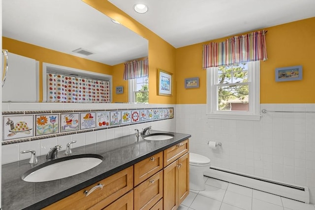 bathroom featuring a sink, tile walls, baseboard heating, and visible vents