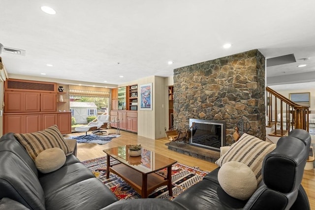 living room featuring stairs, light wood-type flooring, visible vents, recessed lighting, and a fireplace