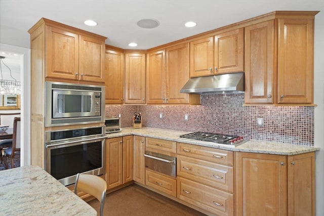 kitchen with a warming drawer, light stone counters, stainless steel appliances, and under cabinet range hood