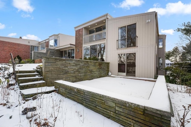 snow covered rear of property featuring a balcony and fence