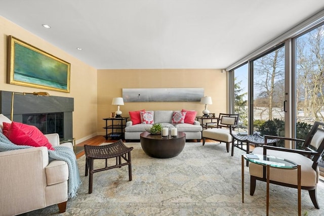 living area with baseboards, a glass covered fireplace, wood finished floors, a wall of windows, and recessed lighting