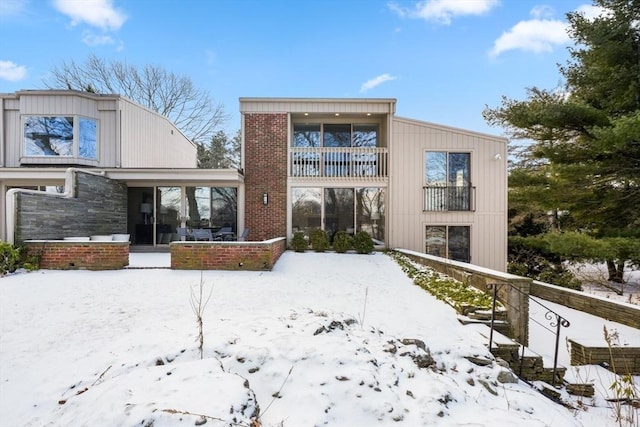 snow covered back of property featuring a balcony and a sunroom