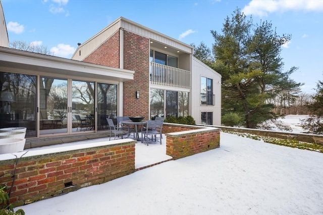 snow covered back of property featuring brick siding, a patio, and a balcony