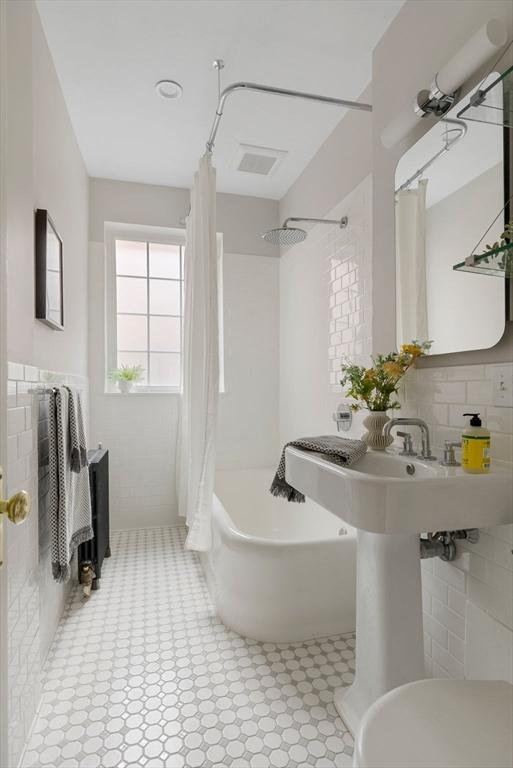 bathroom with toilet, tile walls, and shower / tub combo with curtain