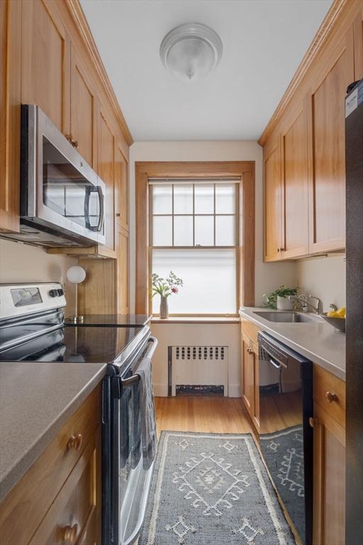 kitchen featuring appliances with stainless steel finishes, radiator heating unit, light wood-type flooring, and a sink