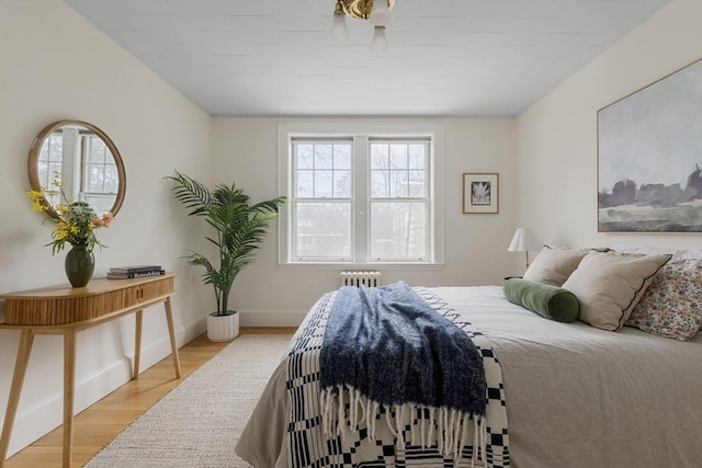 bedroom with radiator, light wood-style flooring, and baseboards