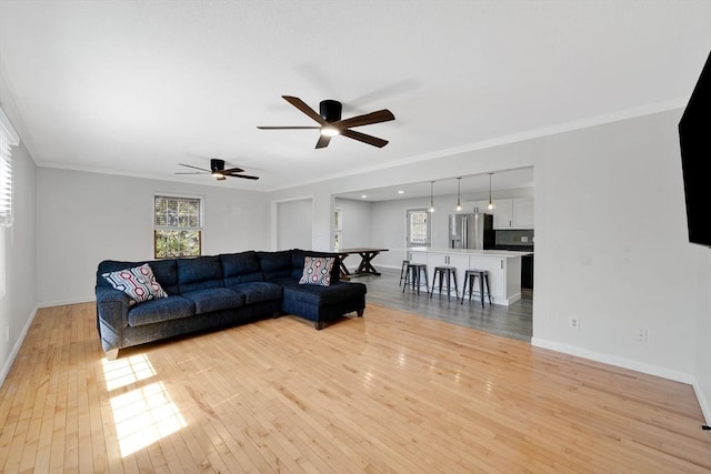 living area featuring light wood-style floors, baseboards, ceiling fan, and crown molding