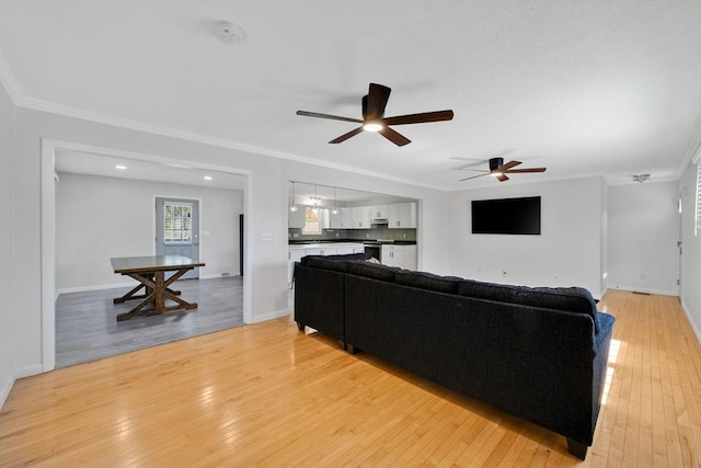 living room featuring baseboards, a ceiling fan, light wood-style flooring, and ornamental molding