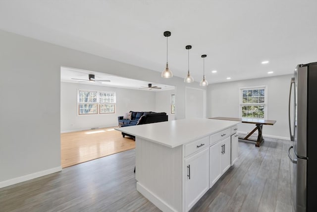 kitchen with light wood-style flooring, a center island, freestanding refrigerator, white cabinetry, and baseboards