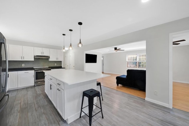 kitchen featuring electric range, ceiling fan, white cabinetry, light wood-type flooring, and a kitchen bar