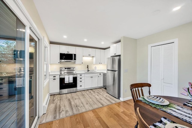 kitchen with a sink, stainless steel appliances, light wood-style floors, and white cabinetry