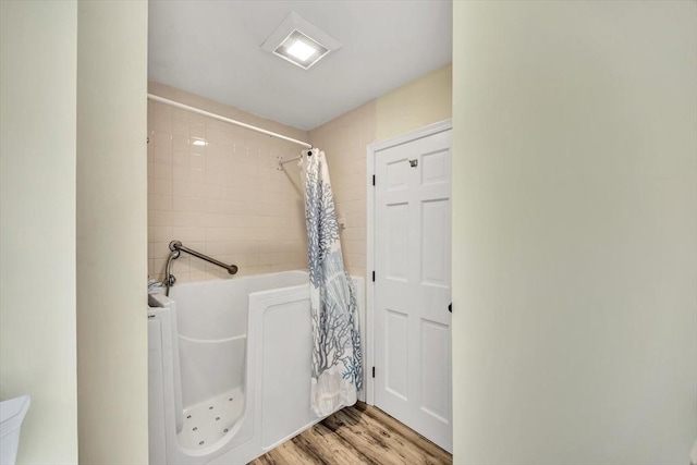 bathroom with a bathing tub, curtained shower, and wood finished floors