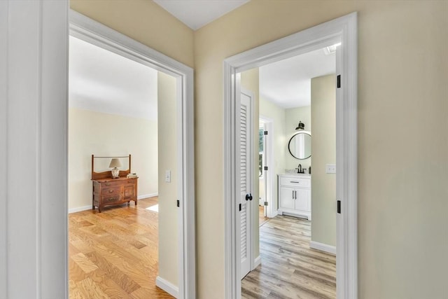 corridor with baseboards, light wood finished floors, and a sink