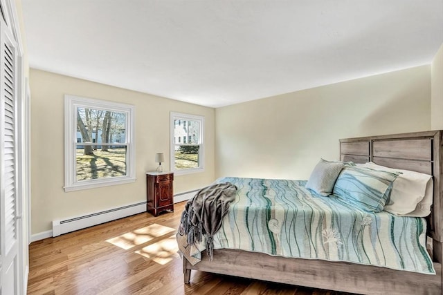 bedroom featuring a baseboard heating unit, baseboards, and wood finished floors