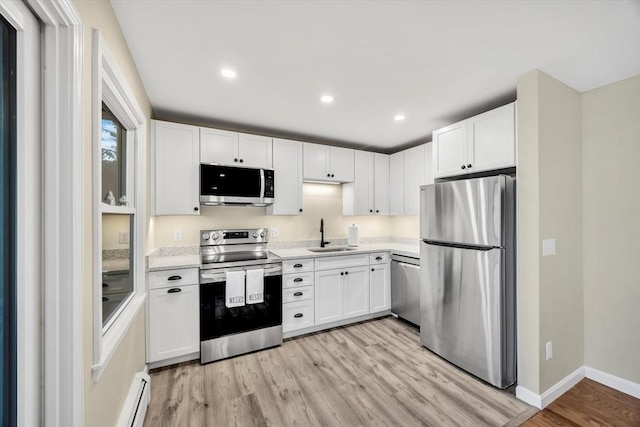 kitchen featuring light wood-type flooring, a sink, white cabinetry, stainless steel appliances, and light countertops